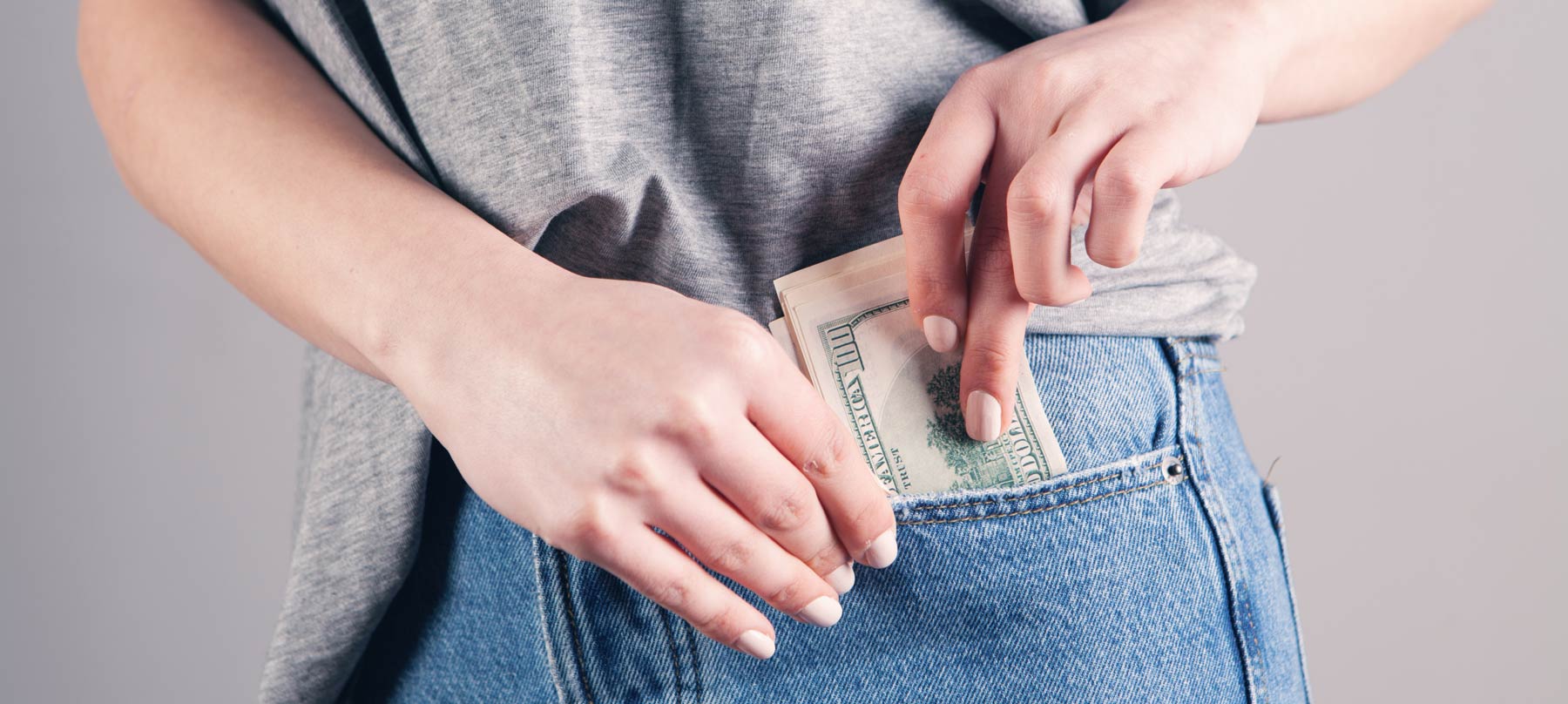 Woman putting 100 dollar bills in jeans pocket